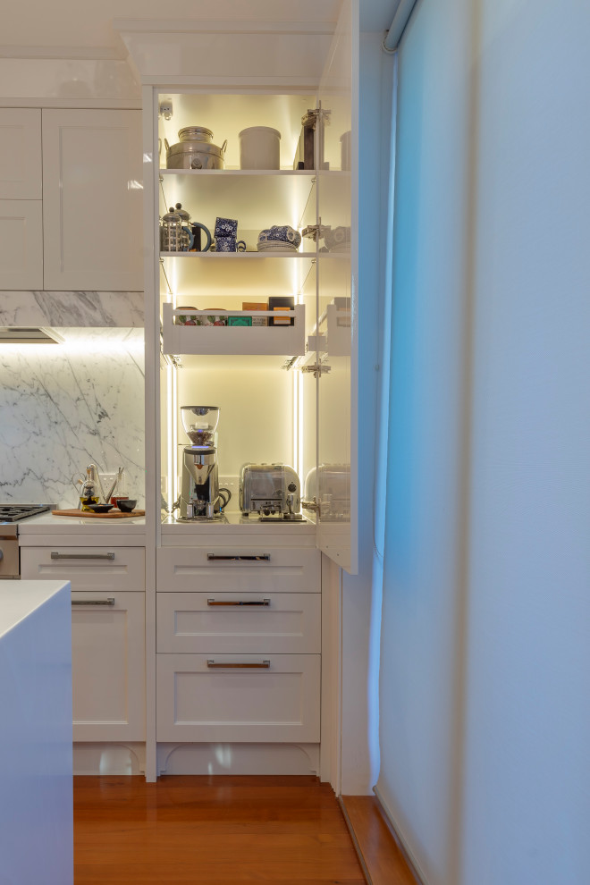 This is an example of a mid-sized transitional single-wall eat-in kitchen in Auckland with an undermount sink, recessed-panel cabinets, white cabinets, solid surface benchtops, grey splashback, marble splashback, stainless steel appliances, medium hardwood floors, with island, brown floor and white benchtop.