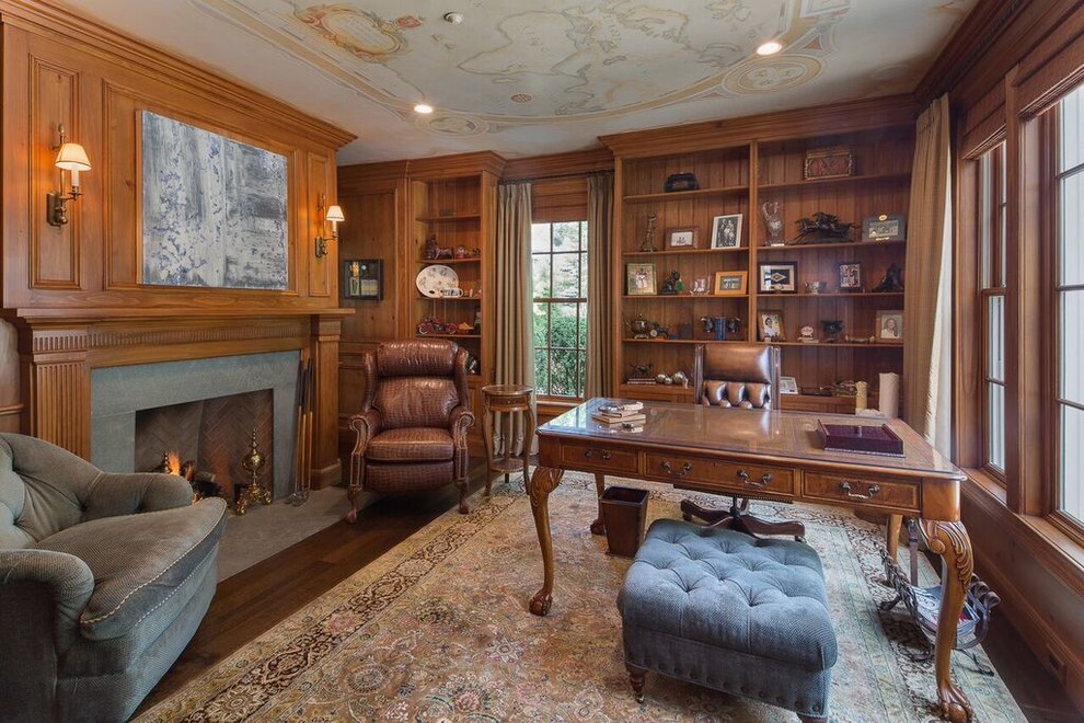 Inspiration for a mid-sized traditional study room in New York with brown walls, dark hardwood floors, a standard fireplace, a concrete fireplace surround, a freestanding desk and brown floor.