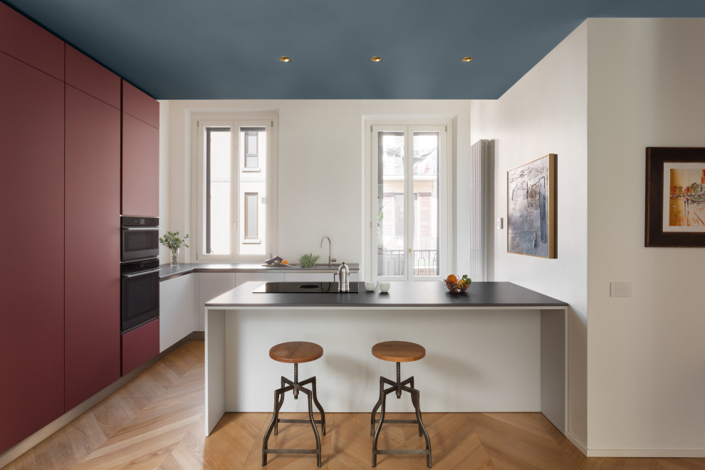 Immagine di una grande cucina design con ante rosse, top in granito, elettrodomestici neri, pavimento in legno massello medio, penisola, top nero e abbinamento di mobili antichi e moderni