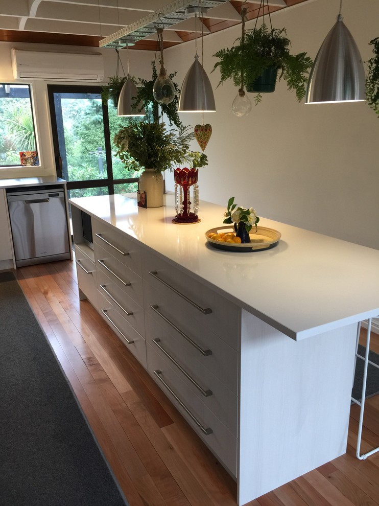 Photo of a large contemporary galley open plan kitchen in Christchurch with a double-bowl sink, flat-panel cabinets, light wood cabinets, quartz benchtops, white splashback, glass sheet splashback, stainless steel appliances, medium hardwood floors, with island and brown floor.