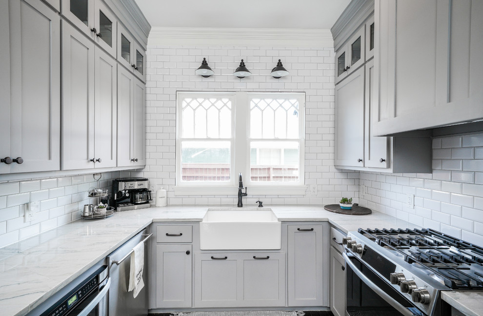 Example of a transitional u-shaped kitchen design with a farmhouse sink, shaker cabinets, gray cabinets, white backsplash, subway tile backsplash, stainless steel appliances, no island and white countertops