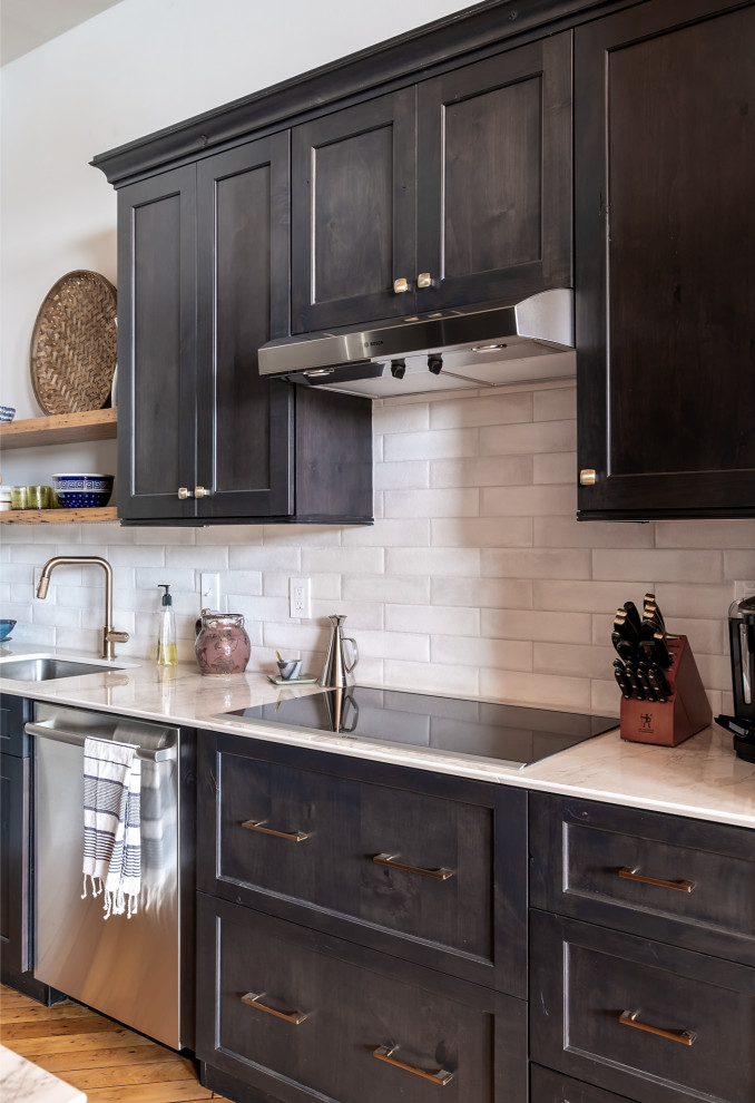 This is an example of an industrial kitchen in Portland Maine with an undermount sink, shaker cabinets, black cabinets, quartz benchtops, white splashback, subway tile splashback, stainless steel appliances, light hardwood floors and white benchtop.