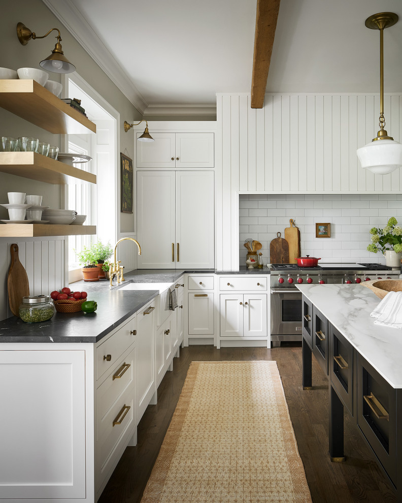 Inspiration for a large transitional u-shaped medium tone wood floor kitchen remodel in Chicago with a farmhouse sink, shaker cabinets, white cabinets, quartzite countertops, white backsplash, subway tile backsplash, paneled appliances, an island and black countertops