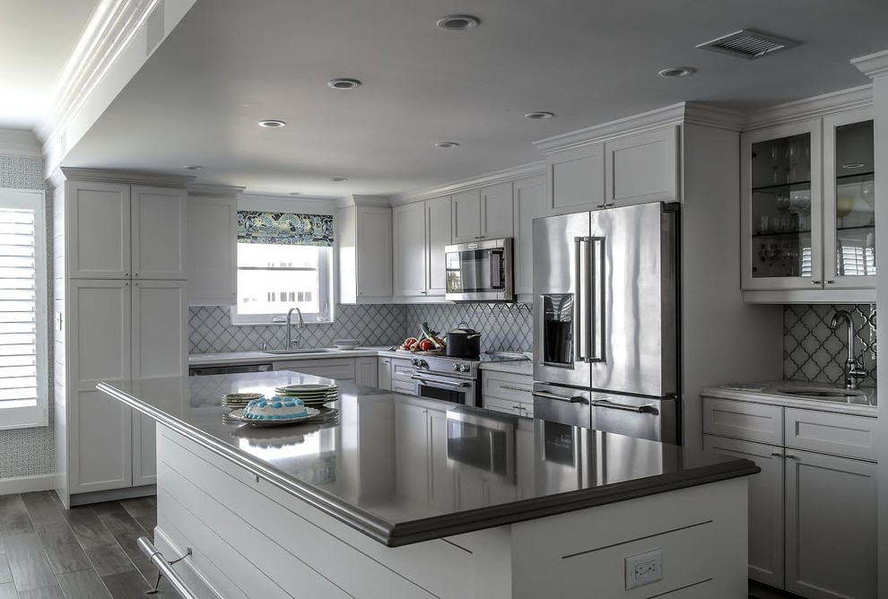 Mid-sized transitional u-shaped dark wood floor and gray floor eat-in kitchen photo in Miami with an undermount sink, recessed-panel cabinets, white cabinets, quartz countertops, white backsplash, ceramic backsplash, stainless steel appliances, an island and white countertops
