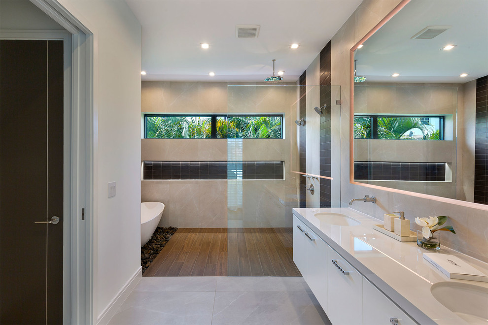 This is an example of a mid-sized modern master bathroom in Miami with flat-panel cabinets, beige cabinets, a freestanding tub, an open shower, a one-piece toilet, beige tile, ceramic tile, beige walls, ceramic floors, an undermount sink, solid surface benchtops, beige floor, an open shower and beige benchtops.