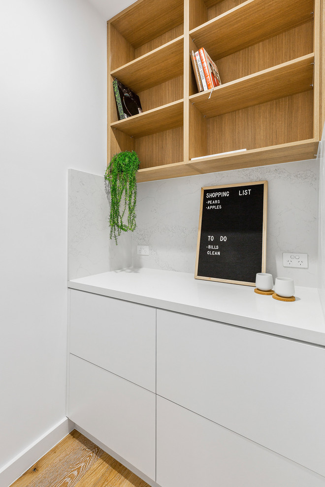 Small contemporary l-shaped kitchen pantry in Melbourne with an undermount sink, white cabinets, quartz benchtops, white splashback, marble splashback, stainless steel appliances, light hardwood floors, with island and white benchtop.