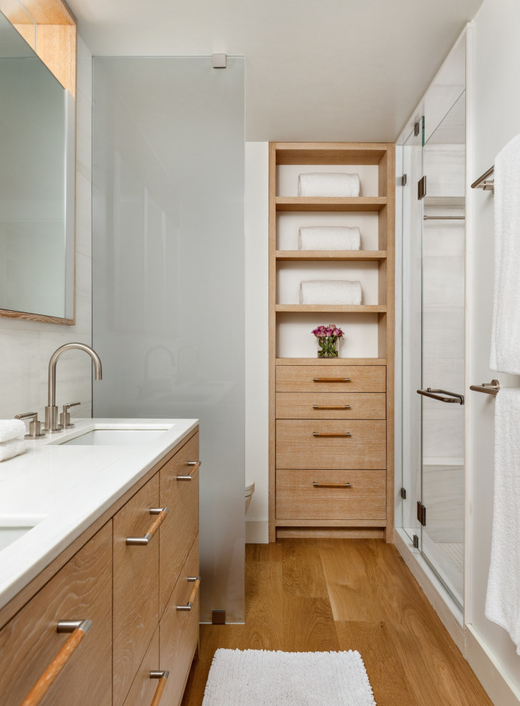 Mid-sized scandinavian master bathroom in New York with flat-panel cabinets, beige cabinets, an alcove shower, a wall-mount toilet, white tile, ceramic tile, white walls, light hardwood floors, an undermount sink, marble benchtops, beige floor, a hinged shower door and white benchtops.