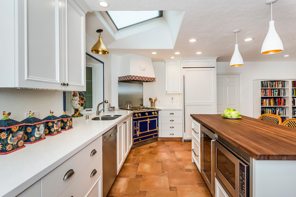 This is an example of a large mediterranean u-shaped open plan kitchen in San Francisco with a double-bowl sink, recessed-panel cabinets, white cabinets, solid surface benchtops, panelled appliances, terra-cotta floors, with island, brown floor and white benchtop.