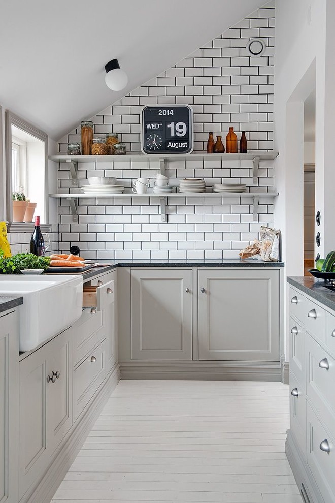 Photo of a small contemporary galley separate kitchen in Madrid with a farmhouse sink, recessed-panel cabinets, grey cabinets, white splashback, subway tile splashback, painted wood floors and no island.