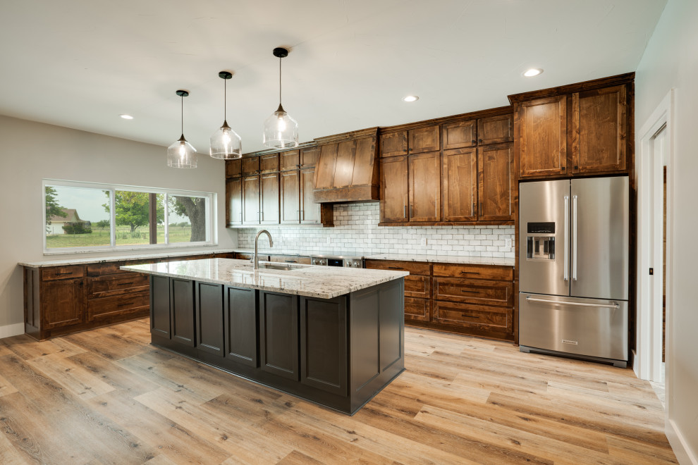 Inspiration for a mid-sized country l-shaped eat-in kitchen in Dallas with an undermount sink, shaker cabinets, medium wood cabinets, granite benchtops, white splashback, subway tile splashback, stainless steel appliances, medium hardwood floors, with island, brown floor, grey benchtop and vaulted.