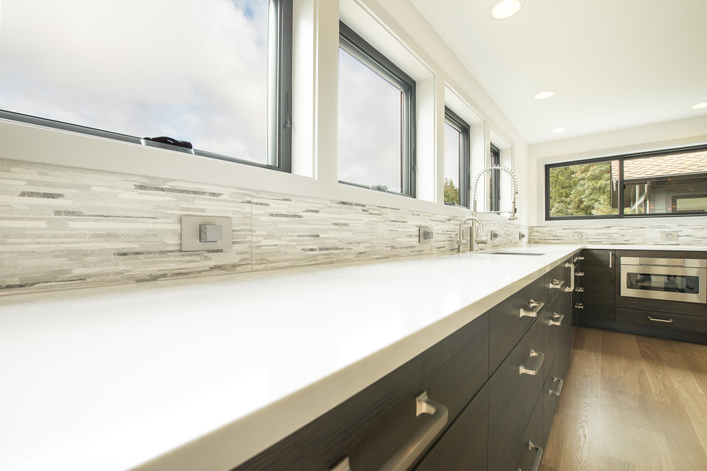 Open concept kitchen - large transitional u-shaped light wood floor and beige floor open concept kitchen idea in Seattle with an undermount sink, flat-panel cabinets, dark wood cabinets, granite countertops, gray backsplash, matchstick tile backsplash, stainless steel appliances, an island and multicolored countertops