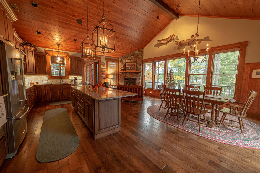 Eat-in kitchen - rustic medium tone wood floor and vaulted ceiling eat-in kitchen idea with a drop-in sink, raised-panel cabinets, medium tone wood cabinets, solid surface countertops, beige backsplash, stone tile backsplash, stainless steel appliances and an island