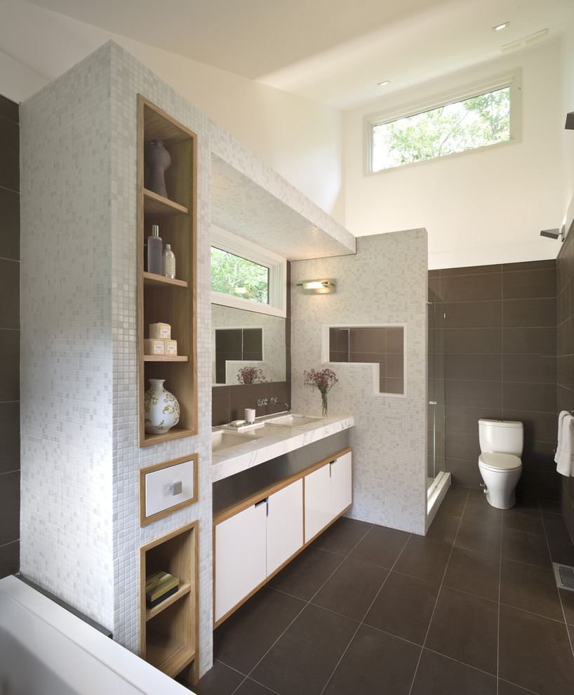 Mid-sized contemporary master bathroom in New York with mosaic tile, an undermount sink, marble benchtops, a drop-in tub, an alcove shower, a one-piece toilet, multi-coloured walls, limestone floors, white cabinets, brown tile and flat-panel cabinets.
