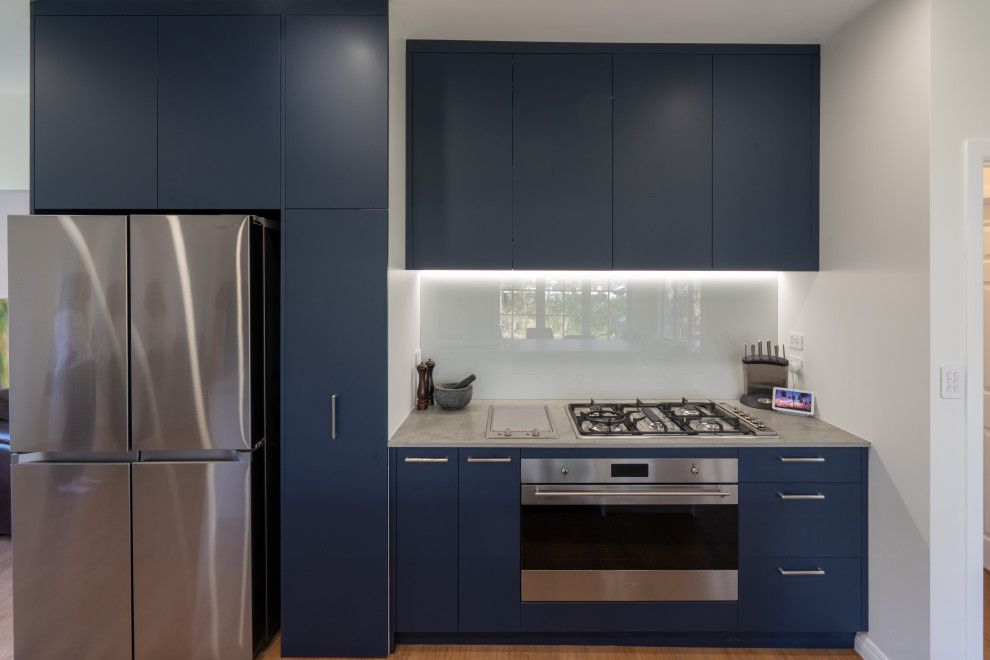 Design ideas for a large transitional galley eat-in kitchen in Auckland with an undermount sink, blue cabinets, white splashback, glass sheet splashback, stainless steel appliances, laminate floors and with island.
