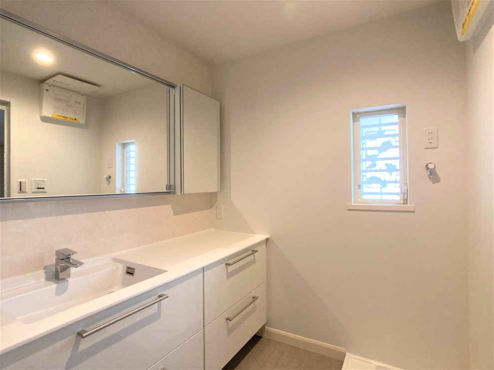 Foto på ett funkis vit toalett, med släta luckor, vita skåp, beige kakel, beige väggar, linoleumgolv, ett integrerad handfat, bänkskiva i akrylsten och brunt golv