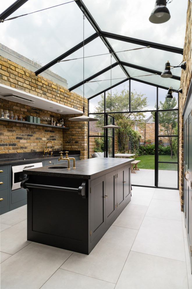 Small industrial galley separate kitchen in London with a drop-in sink, flat-panel cabinets, green cabinets, granite benchtops, beige splashback, brick splashback, panelled appliances, limestone floors, with island, beige floor and black benchtop.