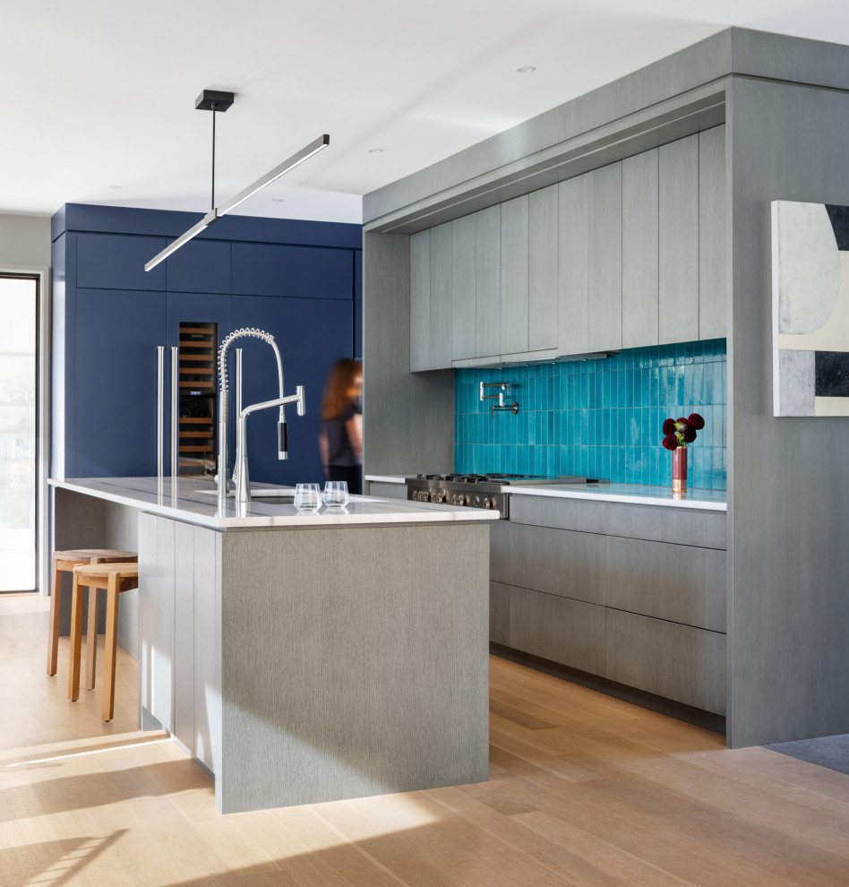 Inspiration for a large contemporary single-wall eat-in kitchen in Portland Maine with a single-bowl sink, flat-panel cabinets, grey cabinets, marble benchtops, brown splashback, ceramic splashback, stainless steel appliances, light hardwood floors, with island, beige floor and white benchtop.