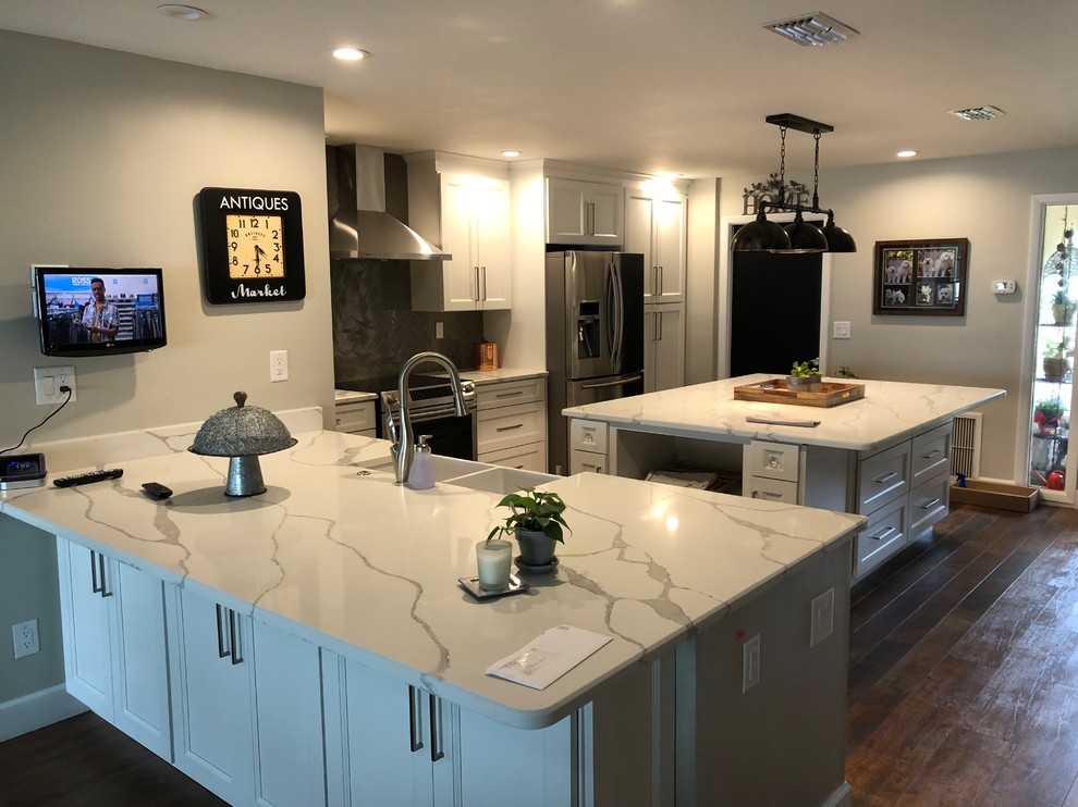 Inspiration for a large transitional u-shaped dark wood floor and brown floor enclosed kitchen remodel in Tampa with a farmhouse sink, shaker cabinets, white cabinets, quartzite countertops, black backsplash, ceramic backsplash, stainless steel appliances, an island and white countertops