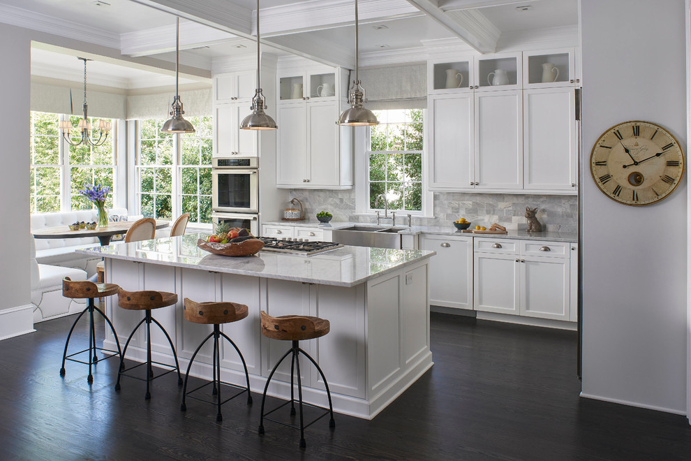Inspiration for a mid-sized transitional l-shaped open plan kitchen in Orlando with a farmhouse sink, shaker cabinets, white cabinets, marble benchtops, subway tile splashback, stainless steel appliances, dark hardwood floors, with island and grey splashback.