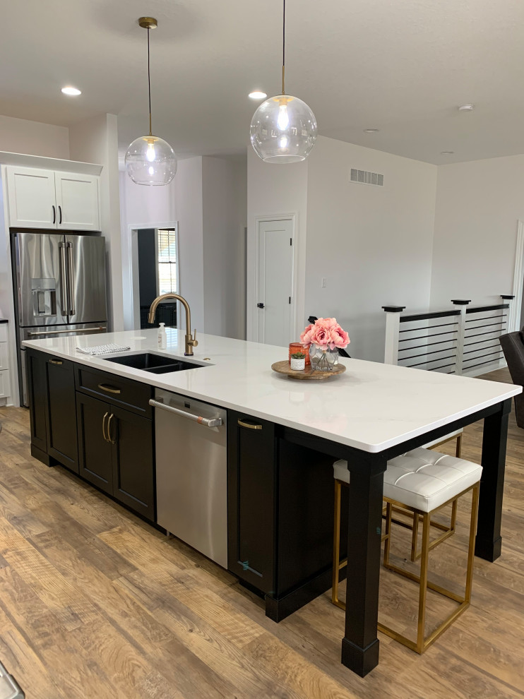 Large transitional l-shaped open plan kitchen in Other with an undermount sink, recessed-panel cabinets, white cabinets, quartz benchtops, white splashback, ceramic splashback, stainless steel appliances, vinyl floors, with island, brown floor and white benchtop.