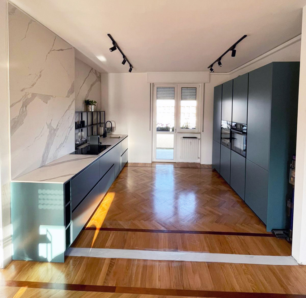 Photo of a mid-sized modern galley open plan kitchen in Milan with an integrated sink, flat-panel cabinets, green cabinets, marble benchtops, white splashback, marble splashback, black appliances, light hardwood floors, no island, beige floor and white benchtop.