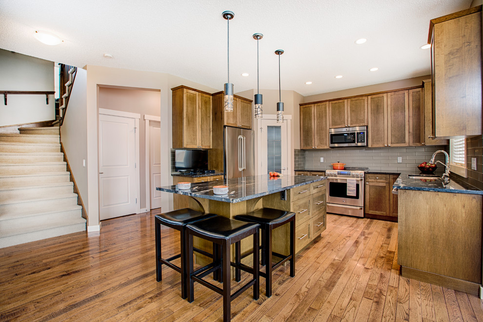 Inspiration for a mid-sized rustic u-shaped medium tone wood floor and brown floor eat-in kitchen remodel in Calgary with an undermount sink, shaker cabinets, medium tone wood cabinets, granite countertops, gray backsplash, glass tile backsplash, stainless steel appliances and an island