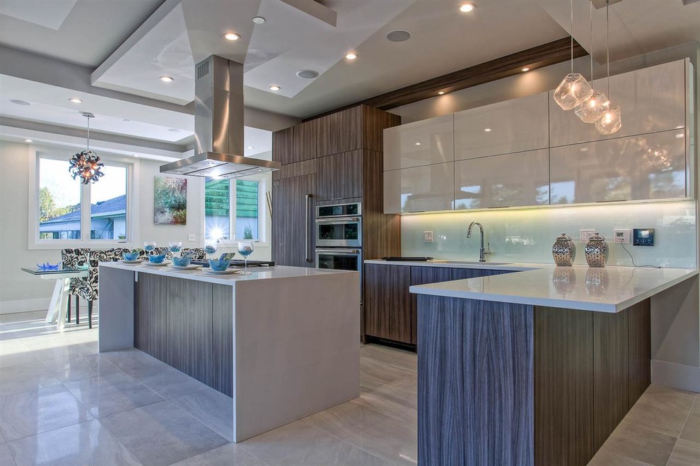 Expansive modern l-shaped eat-in kitchen in Vancouver with a double-bowl sink, glass-front cabinets, brown cabinets, quartz benchtops, white splashback, glass tile splashback, panelled appliances, cement tiles, multiple islands and grey floor.
