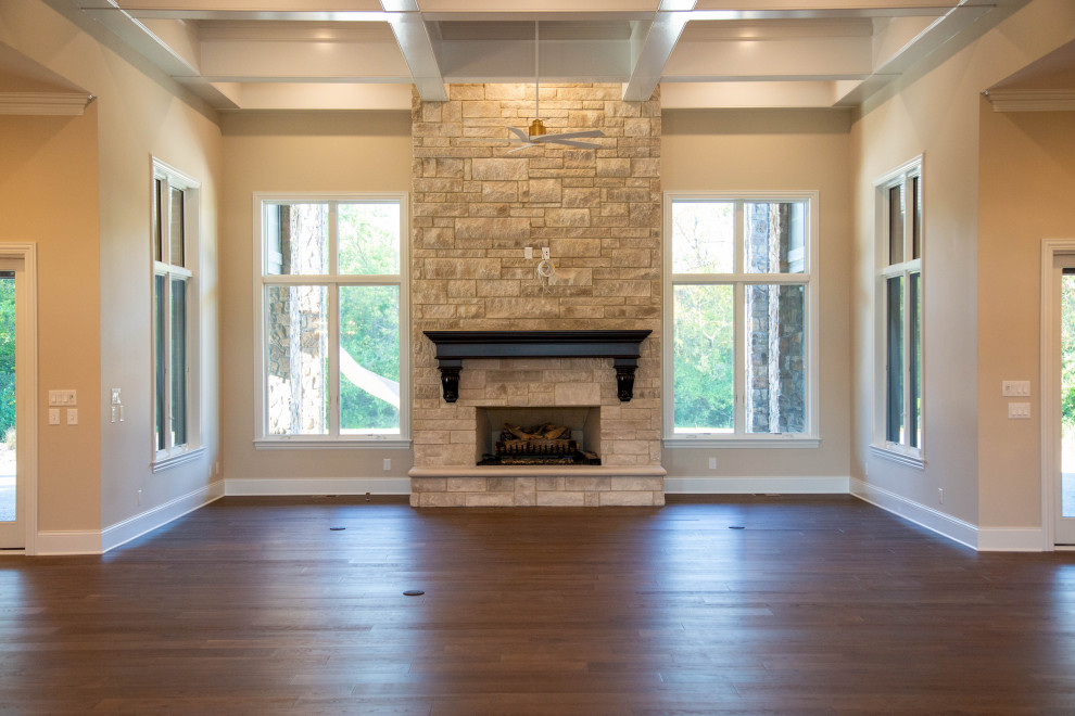 Photo of an expansive transitional open concept living room in Indianapolis with a home bar, beige walls, laminate floors, a standard fireplace, a stone fireplace surround, a wall-mounted tv, brown floor and coffered.