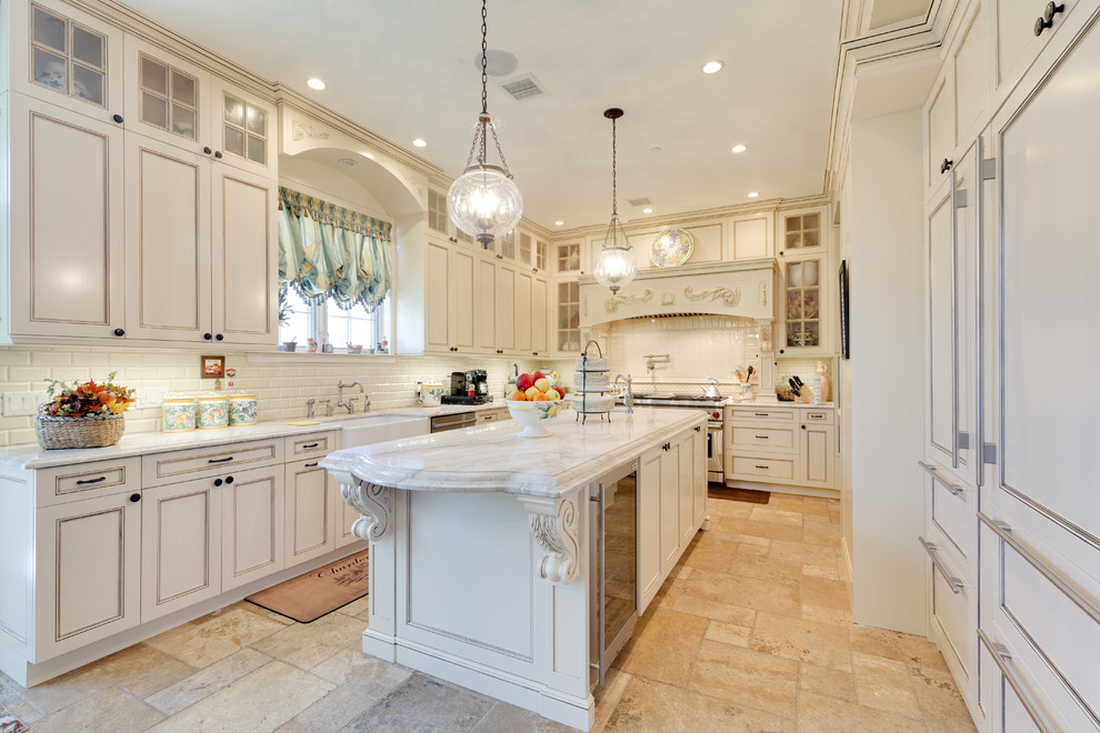 Photo of a traditional u-shaped kitchen in New York with a farmhouse sink, recessed-panel cabinets, beige cabinets, white splashback, subway tile splashback, panelled appliances, with island and beige floor.