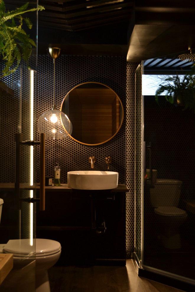 Пример оригинального дизайна: ванная комната среднего размера в стиле неоклассика (современная классика) с угловым душем, черной плиткой, душевой кабиной, столешницей из дерева, душем с распашными дверями, коричневой столешницей, тумбой под одну раковину, унитазом-моноблоком, черными стенами, полом из ламината, настольной раковиной, серым полом и керамогранитной плиткой