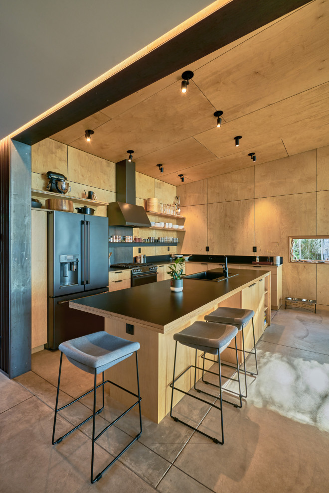 Photo of a country l-shaped open plan kitchen in Seattle with light wood cabinets, timber splashback, black appliances, concrete floors, with island, black benchtop and wood.