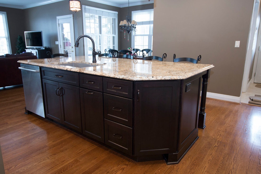 Large traditional l-shaped eat-in kitchen in Cincinnati with an undermount sink, shaker cabinets, black cabinets, granite benchtops, beige splashback, stone tile splashback, stainless steel appliances, medium hardwood floors and with island.