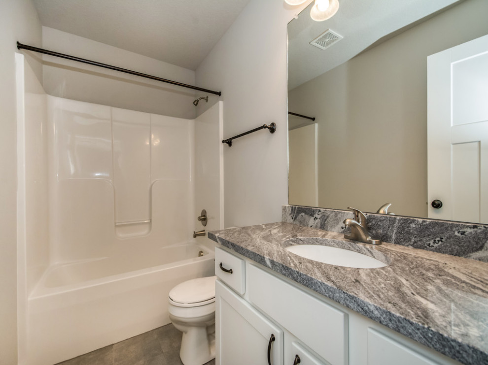 Tub/shower combo - mid-sized transitional 3/4 ceramic tile and gray floor tub/shower combo idea with shaker cabinets, white cabinets, a two-piece toilet, beige walls, an undermount sink, granite countertops and multicolored countertops