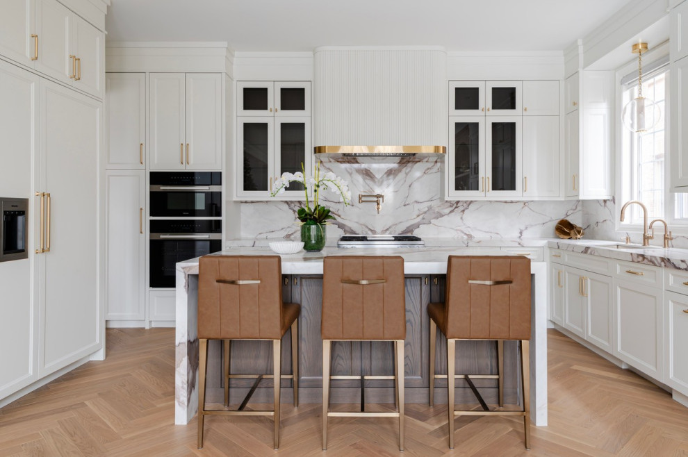 Mid-sized transitional u-shaped medium tone wood floor and brown floor kitchen photo in Toronto with an undermount sink, recessed-panel cabinets, white cabinets, black appliances, an island, white backsplash, stone slab backsplash and white countertops