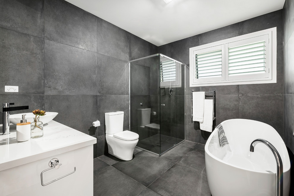 Inspiration for a contemporary master bathroom in Melbourne with a freestanding tub, a corner shower, a two-piece toilet, grey walls, a vessel sink, grey floor and a hinged shower door.