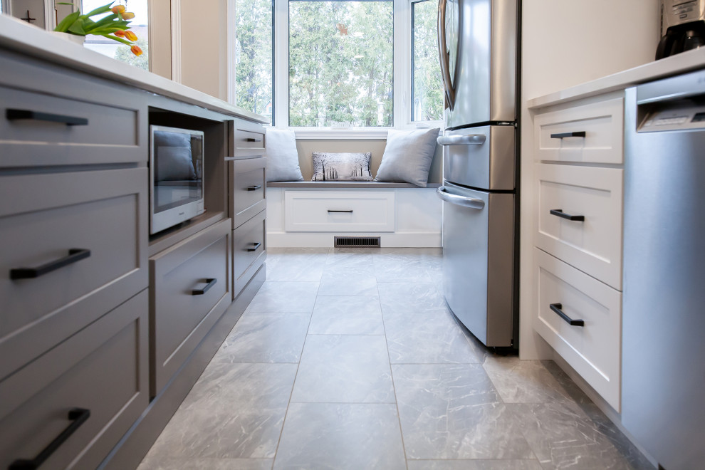 Example of a mid-sized transitional l-shaped gray floor enclosed kitchen design with an undermount sink, shaker cabinets, white cabinets, quartz countertops, gray backsplash, ceramic backsplash, stainless steel appliances, an island and white countertops