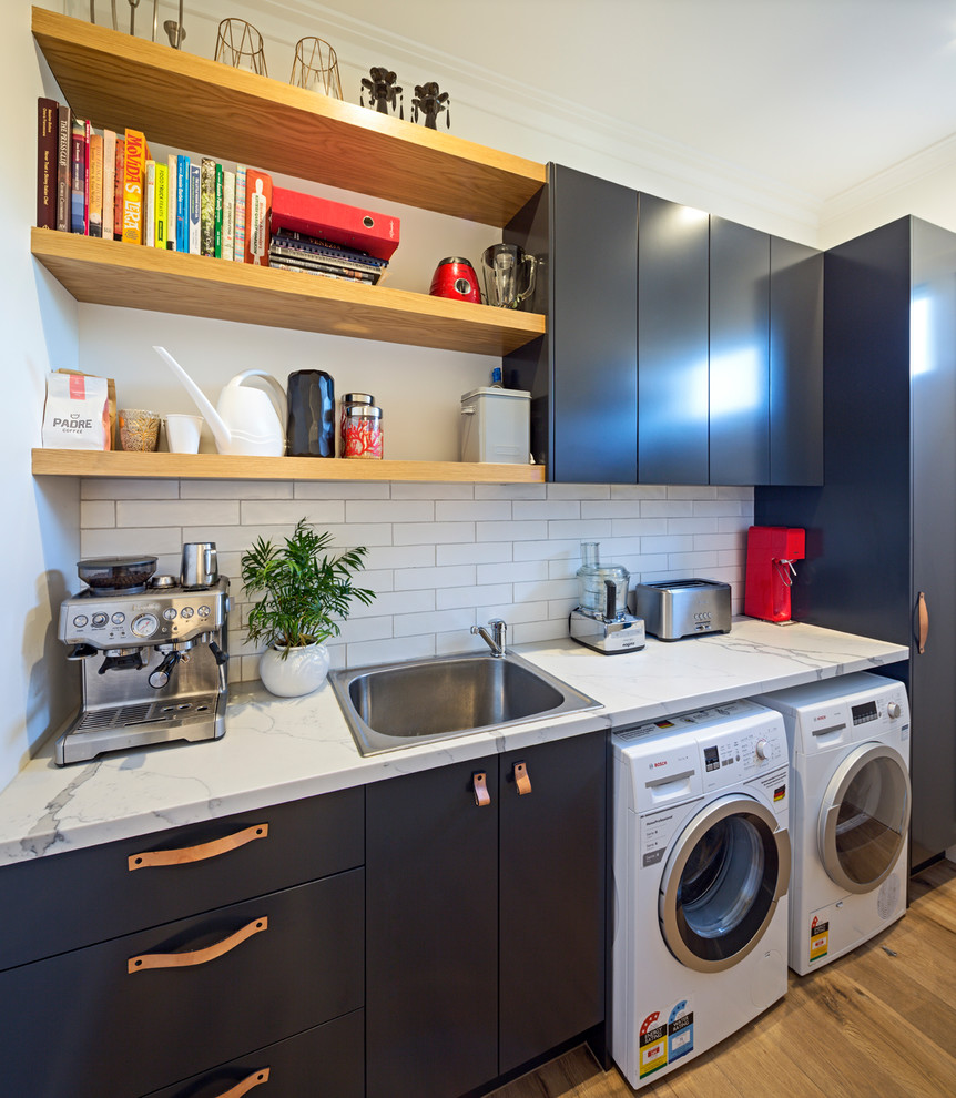 Design ideas for a mid-sized contemporary single-wall dedicated laundry room in Melbourne with a single-bowl sink, flat-panel cabinets, black cabinets, quartz benchtops, white walls, light hardwood floors, yellow floor and white benchtop.