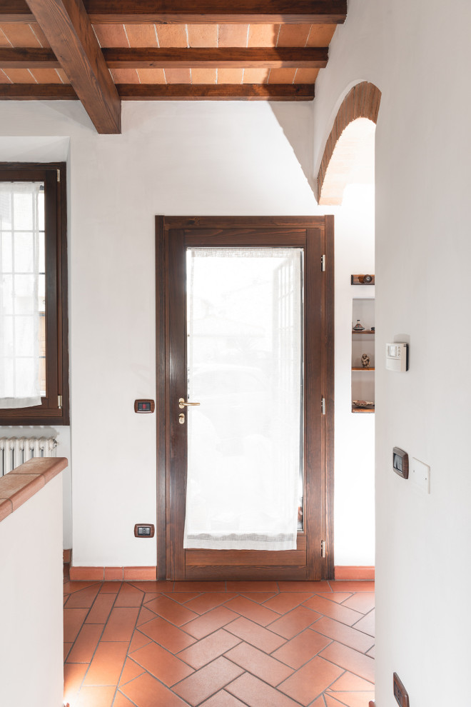 Inspiration pour une petite entrée rustique avec un couloir, un mur blanc, tomettes au sol, une porte simple, une porte en bois foncé, un sol orange et poutres apparentes.