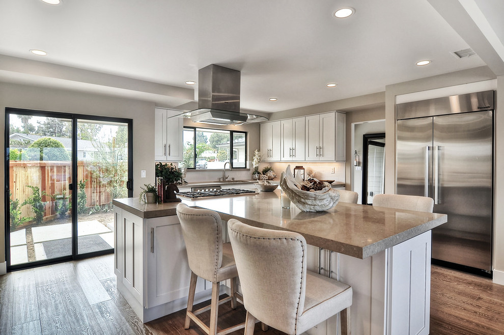 Eat-in kitchen - mid-sized transitional light wood floor eat-in kitchen idea in Orange County with an undermount sink, shaker cabinets, white cabinets, solid surface countertops, white backsplash, ceramic backsplash and stainless steel appliances