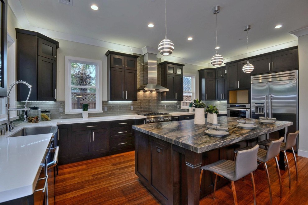 Example of a trendy u-shaped kitchen design in San Francisco with a farmhouse sink, shaker cabinets, dark wood cabinets, gray backsplash, subway tile backsplash, stainless steel appliances and white countertops
