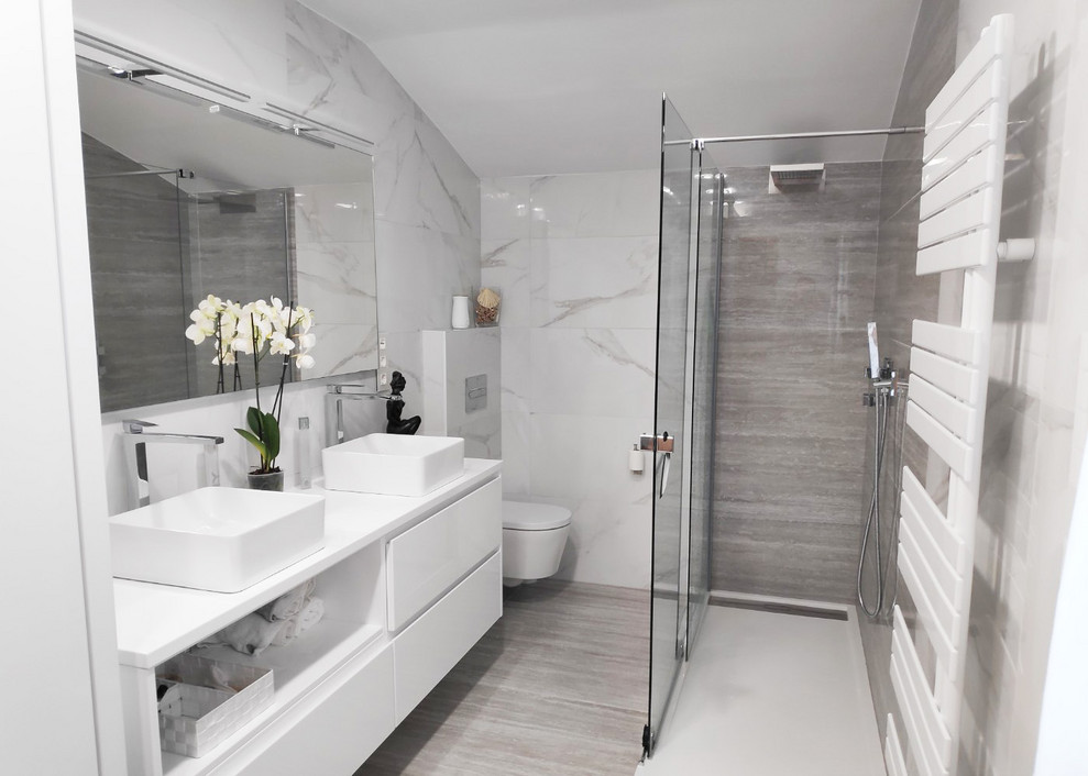 Photo of a mid-sized transitional master bathroom in Bilbao with furniture-like cabinets, white cabinets, an open shower, a wall-mount toilet, black and white tile, ceramic tile, multi-coloured walls, travertine floors, solid surface benchtops, beige floor, a hinged shower door and white benchtops.
