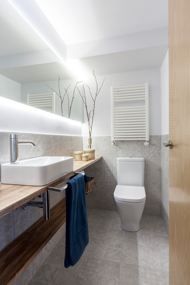 Small contemporary powder room in Madrid with open cabinets, gray tile, white walls, a vessel sink, wood benchtops, grey floor and brown benchtops.