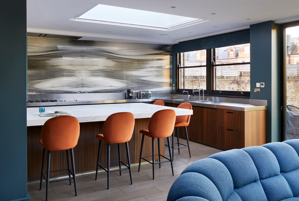 This is an example of a contemporary kitchen in London with a drop-in sink, flat-panel cabinets, dark wood cabinets, stainless steel benchtops, metallic splashback, glass tile splashback, stainless steel appliances, porcelain floors, with island, beige floor and beige benchtop.
