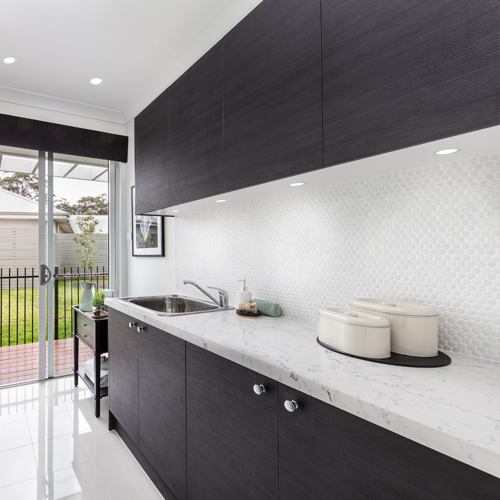 Photo of a large traditional galley dedicated laundry room in Sydney with a drop-in sink, shaker cabinets, brown cabinets, quartz benchtops, white walls, ceramic floors, a concealed washer and dryer, white floor and white benchtop.