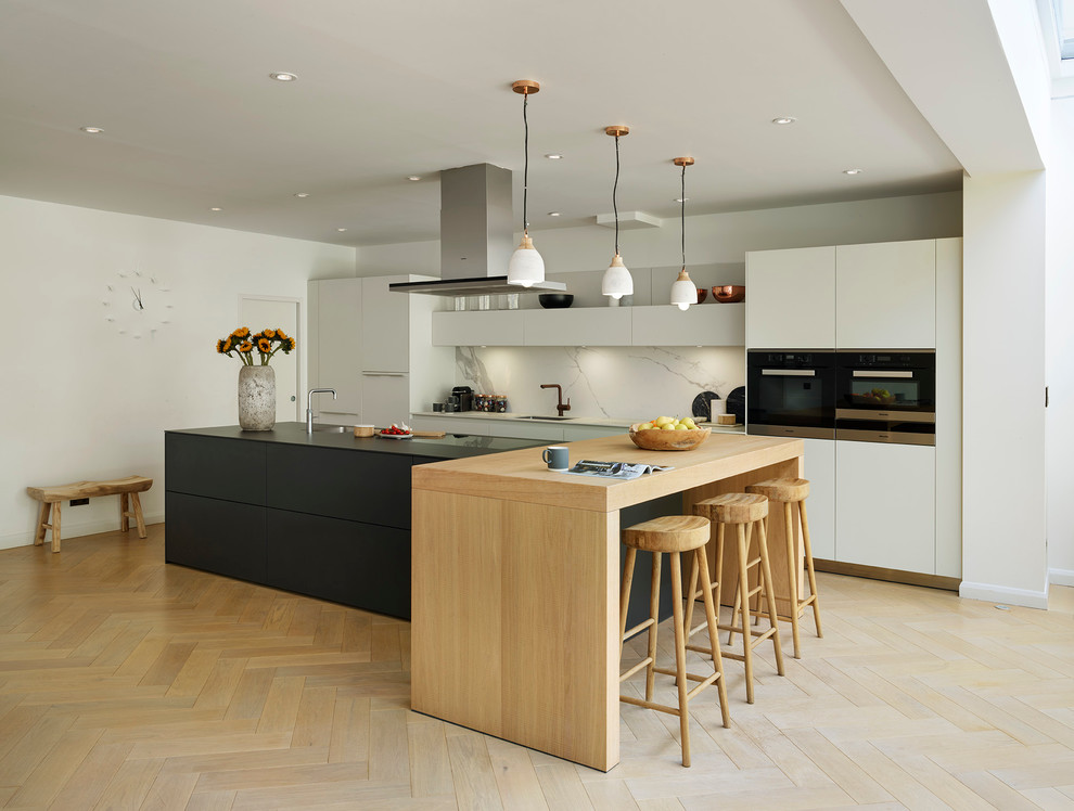 Inspiration for a large contemporary kitchen in Other with an undermount sink, flat-panel cabinets, white cabinets, white splashback, stone slab splashback, black appliances, light hardwood floors and with island.