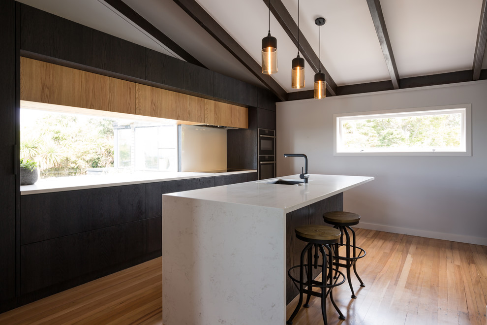 Design ideas for a mid-sized contemporary l-shaped eat-in kitchen in Auckland with quartz benchtops, white splashback, glass sheet splashback, panelled appliances, medium hardwood floors, with island, an undermount sink, flat-panel cabinets, medium wood cabinets and brown floor.