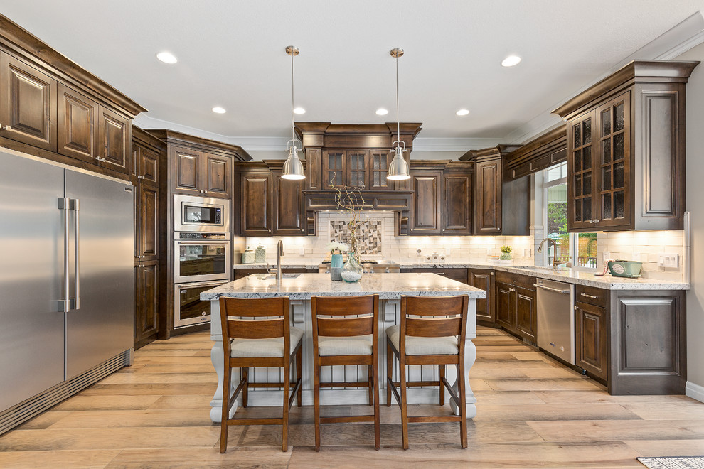 Photo of a transitional u-shaped kitchen in Salt Lake City with an undermount sink, raised-panel cabinets, dark wood cabinets, white splashback, stainless steel appliances, light hardwood floors, with island, beige floor and white benchtop.