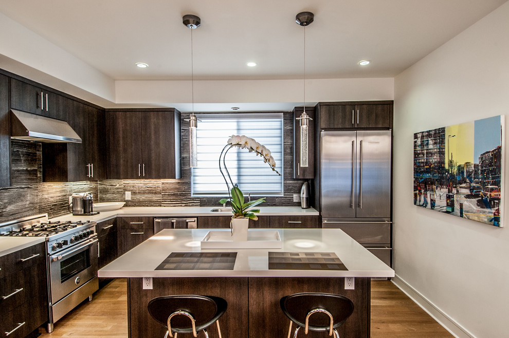 Photo of a small modern l-shaped eat-in kitchen in Los Angeles with a double-bowl sink, flat-panel cabinets, dark wood cabinets, quartz benchtops, grey splashback, stone tile splashback, stainless steel appliances, light hardwood floors and with island.