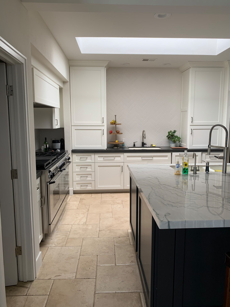 Large transitional travertine floor and beige floor kitchen photo in Orange County with a single-bowl sink, shaker cabinets, white cabinets, quartzite countertops, white backsplash, ceramic backsplash, stainless steel appliances, an island and black countertops