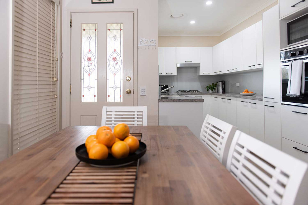 This is an example of a small modern u-shaped kitchen pantry in Melbourne with a double-bowl sink, open cabinets, white cabinets, laminate benchtops, grey splashback, glass sheet splashback, stainless steel appliances, light hardwood floors, no island and grey benchtop.
